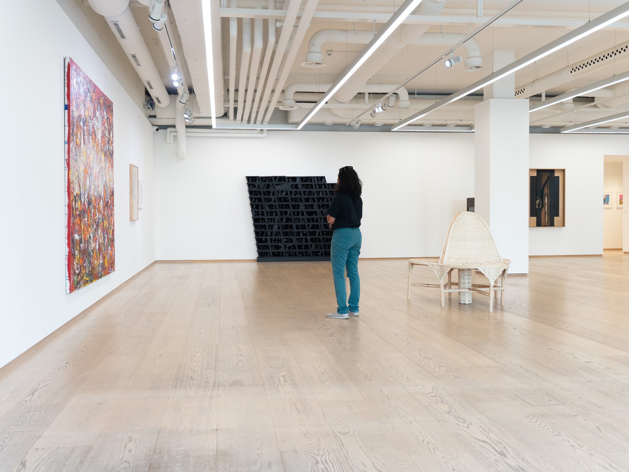 Galerie für zeitgenössische Kunst mit weißen Wänden und hellem Parkett, eine Besucherin vor einem Werk